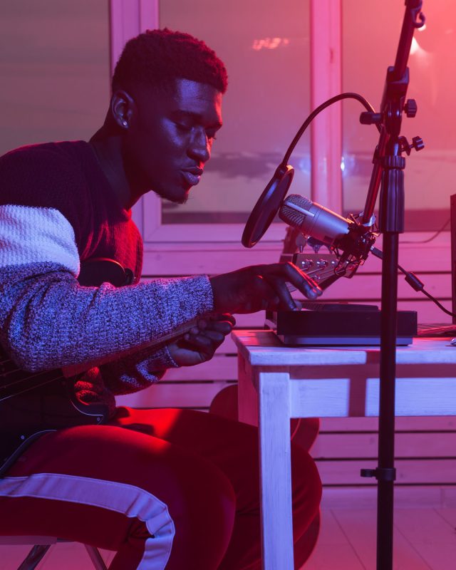 African american professional musician recording guitar in digital studio at home, music production technology concept